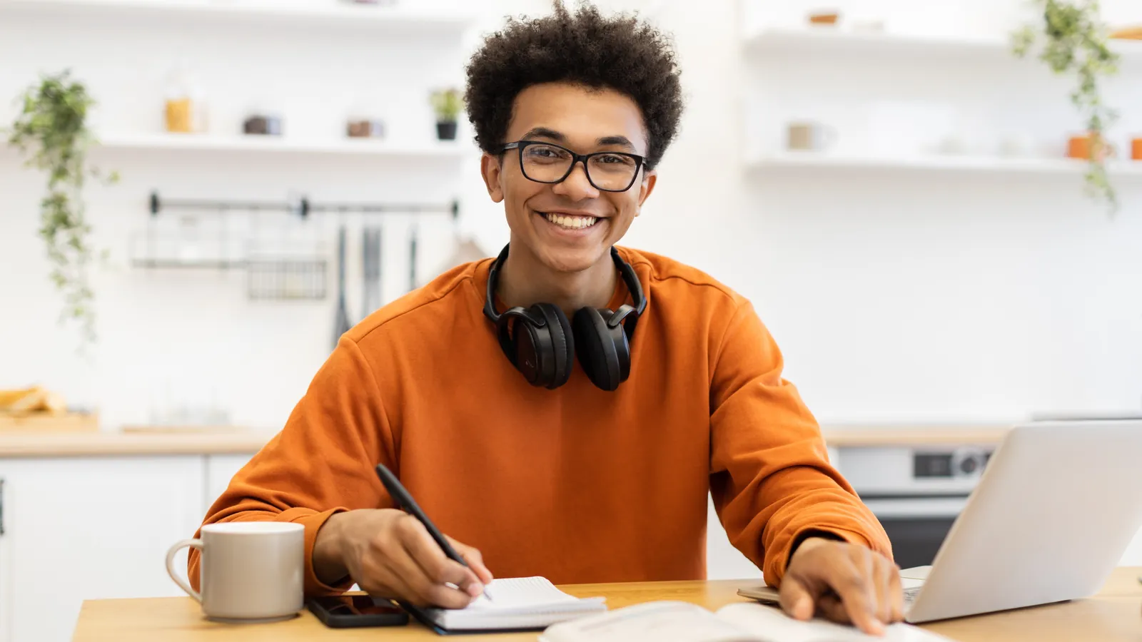 Man met een schrift en laptop aan een studietafel.