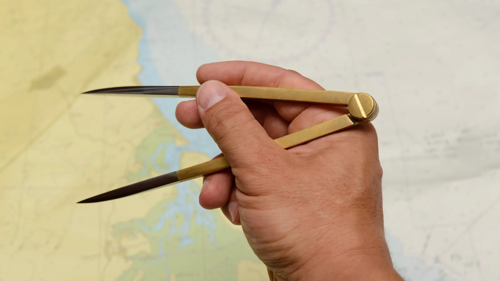 Een hand houdt een navigatiepasser boven een zeekaart.