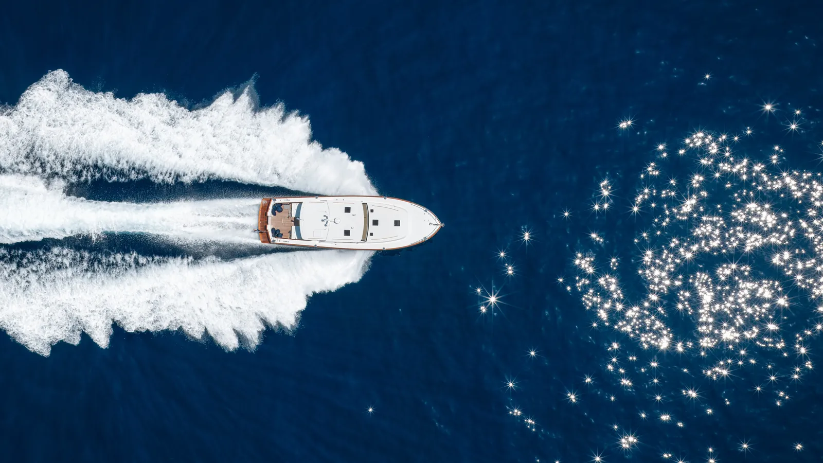 Luchtfoto van een motorboot met een breed kielzog op blauw water.