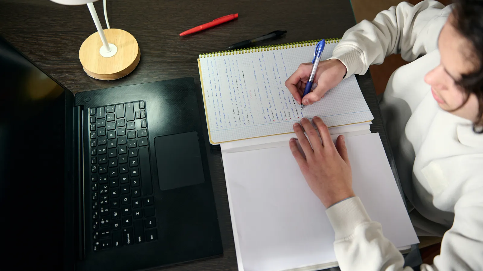 Jongere maakt aantekeningen aan een bureau met een laptop.